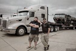 Two men wearing black tshirt in front of a vehicle